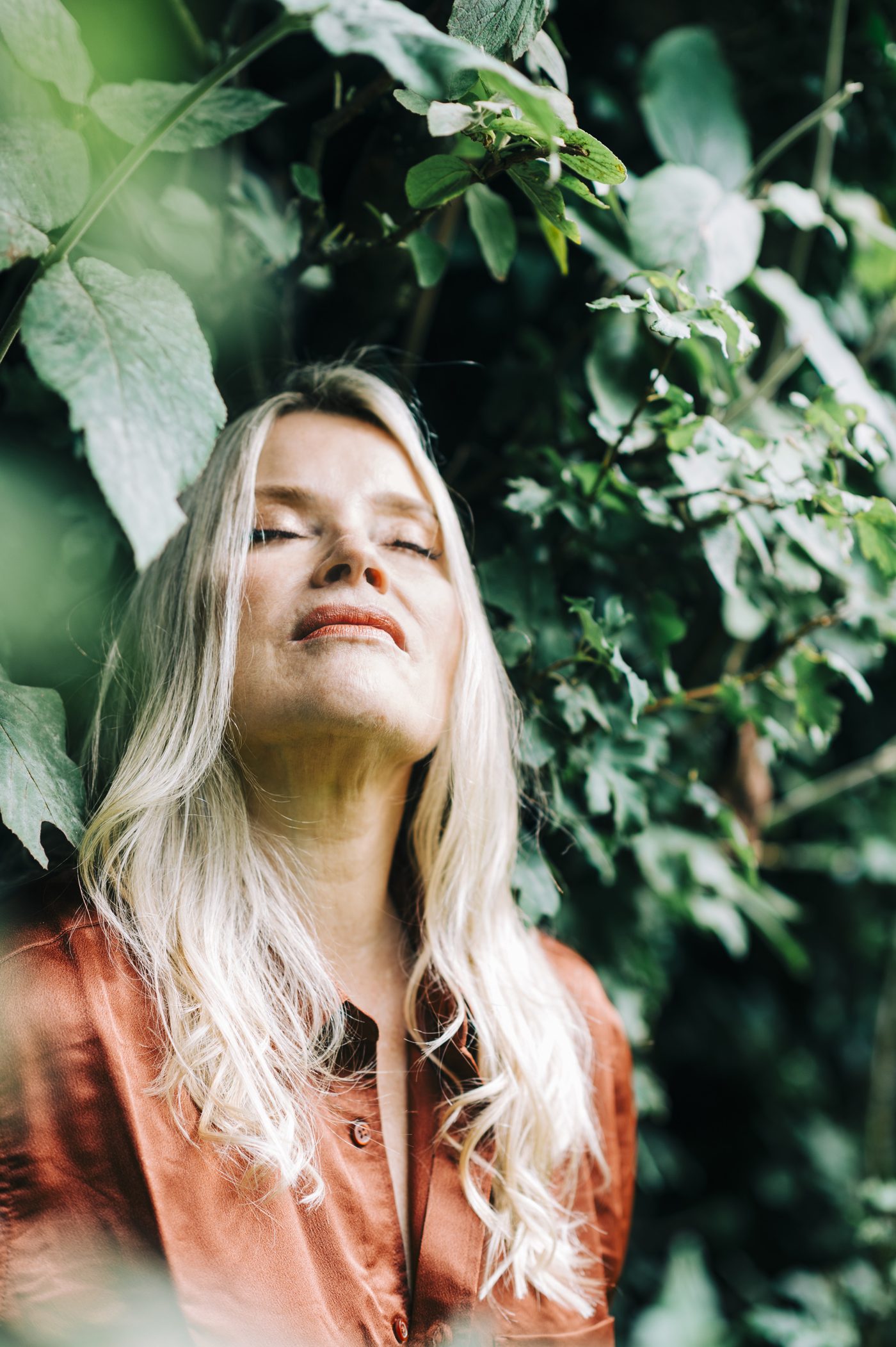 Juliette among green leaves, eyes closed, face tilted up to the light
