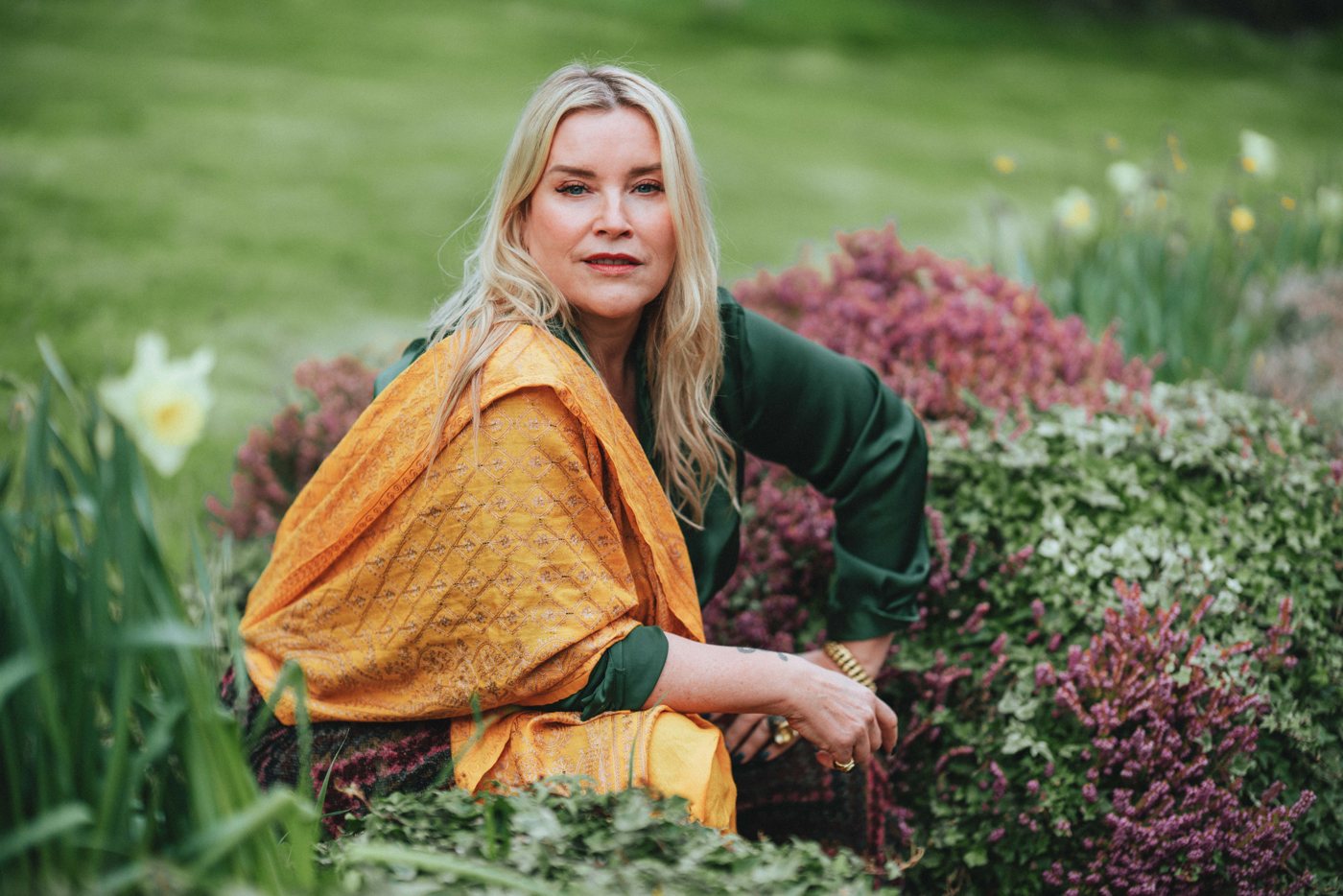 Juliette sitting in a garden among flowers, wrapped in an orange scarf
