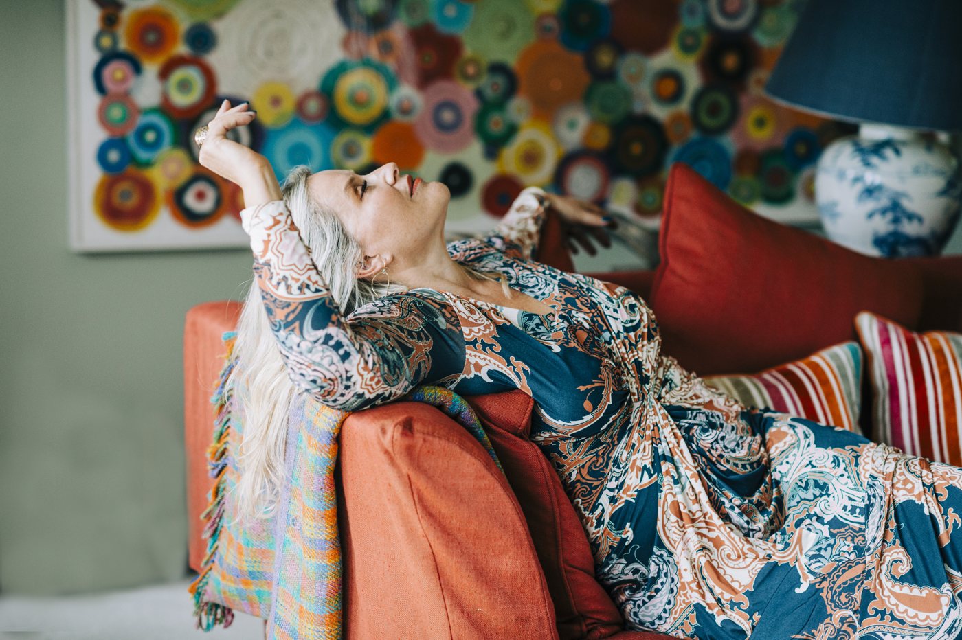 Juliette lying back on a colourful sofa, arms above her head, relaxed