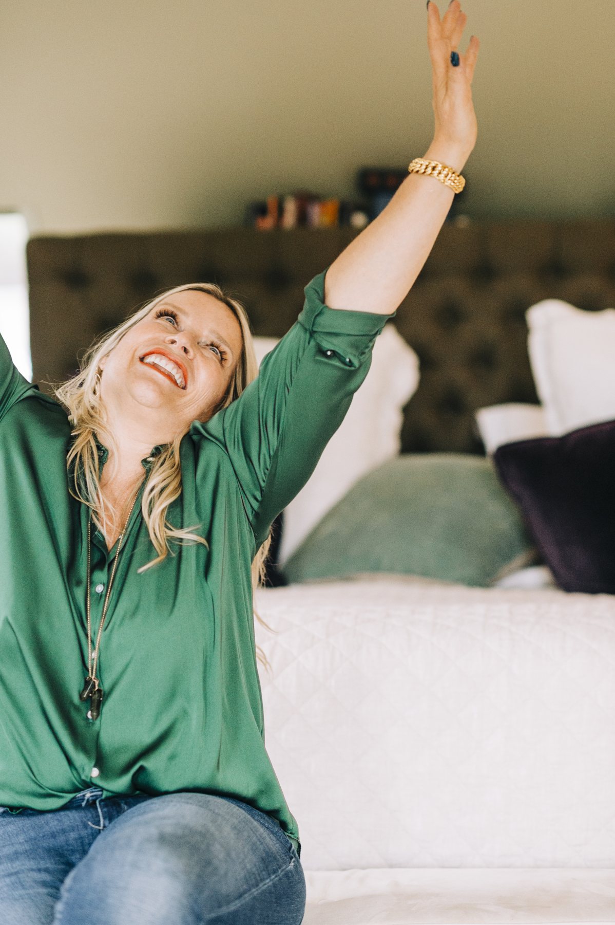Juliette laughing, one arm raised high, sitting on a bed in a green shirt