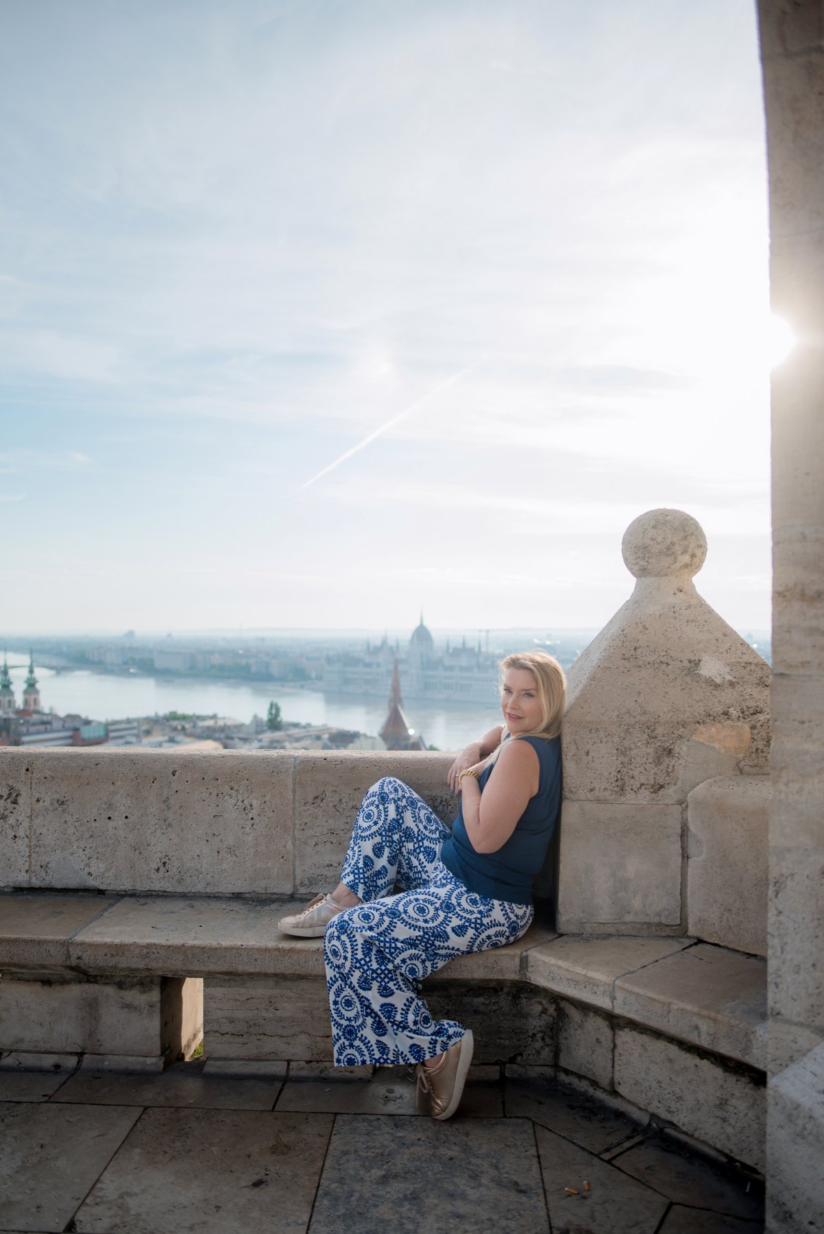 Juliette sitting on a stone balcony above a city and a river at sunrise