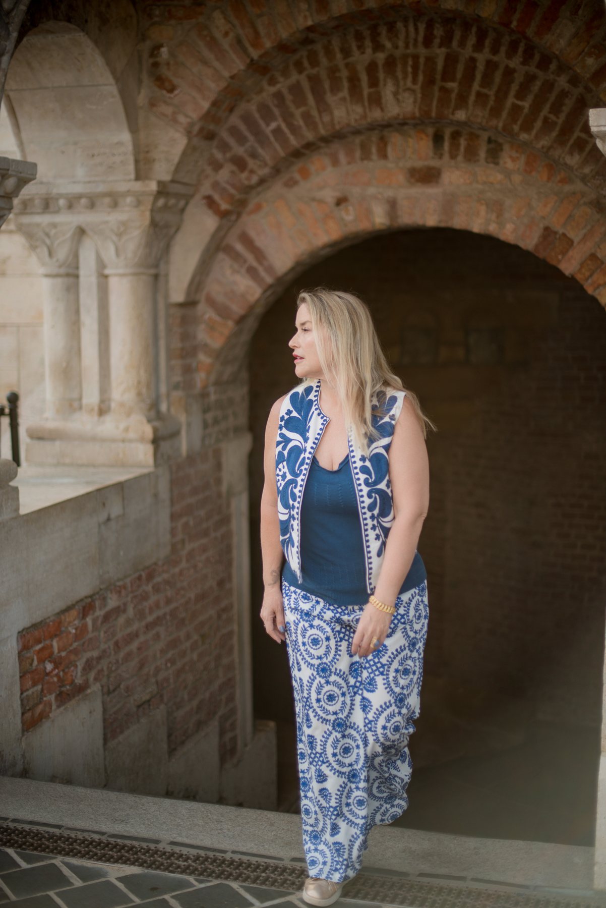 Juliette walking through a stone archway in a blue and white outfit