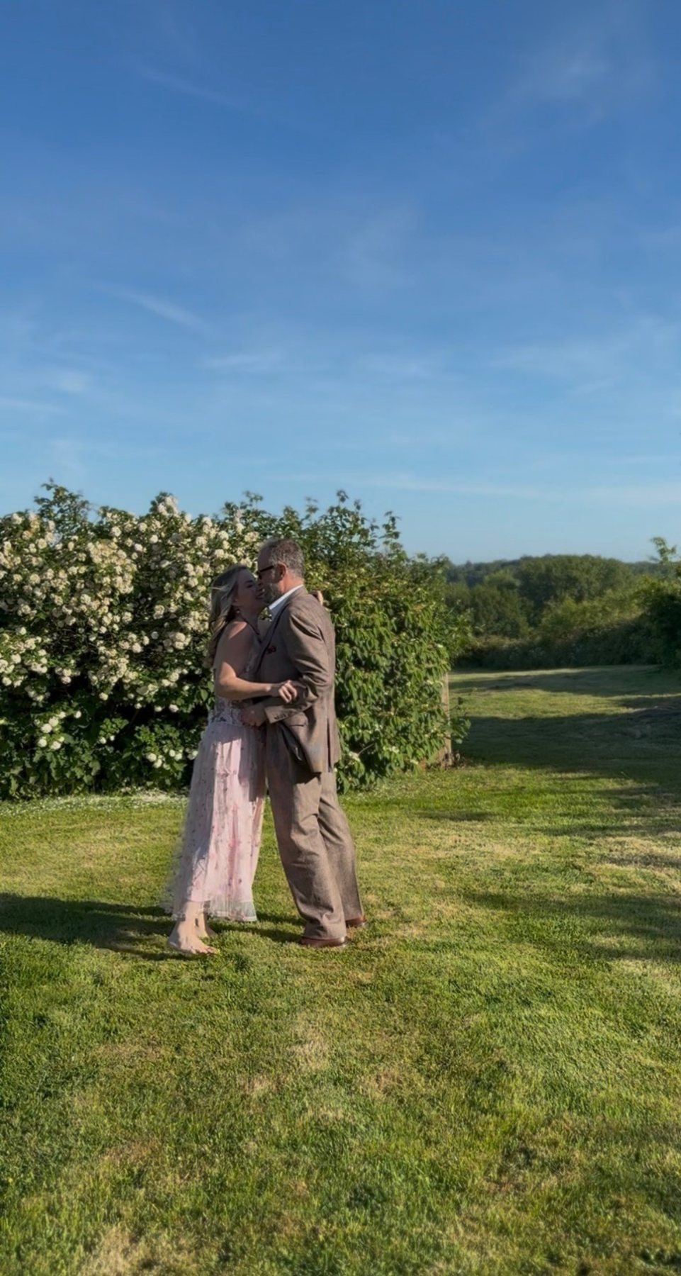 Juliette and Alex holding each other on a lawn in the sun