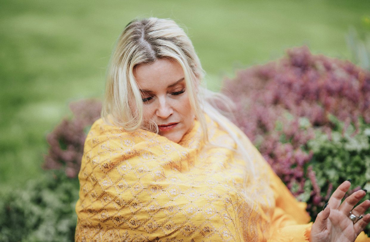 Juliette in a garden, wrapped in a yellow scarf, eyes lowered